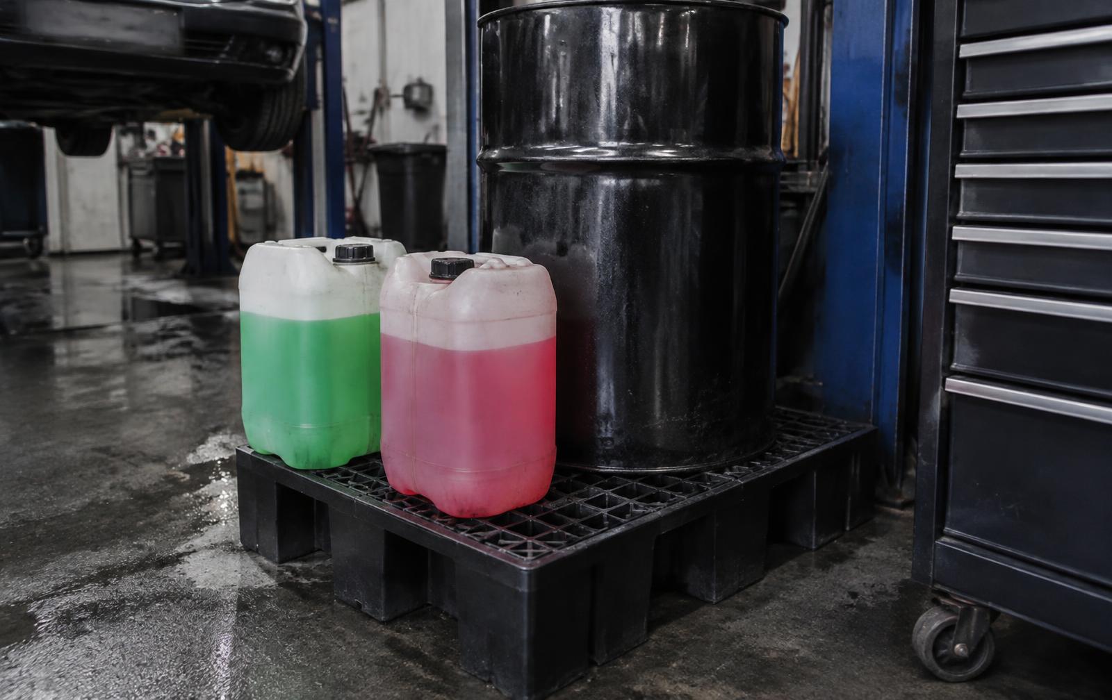 Green and pink waste antifreeze containers on a spill pallet in a workshop