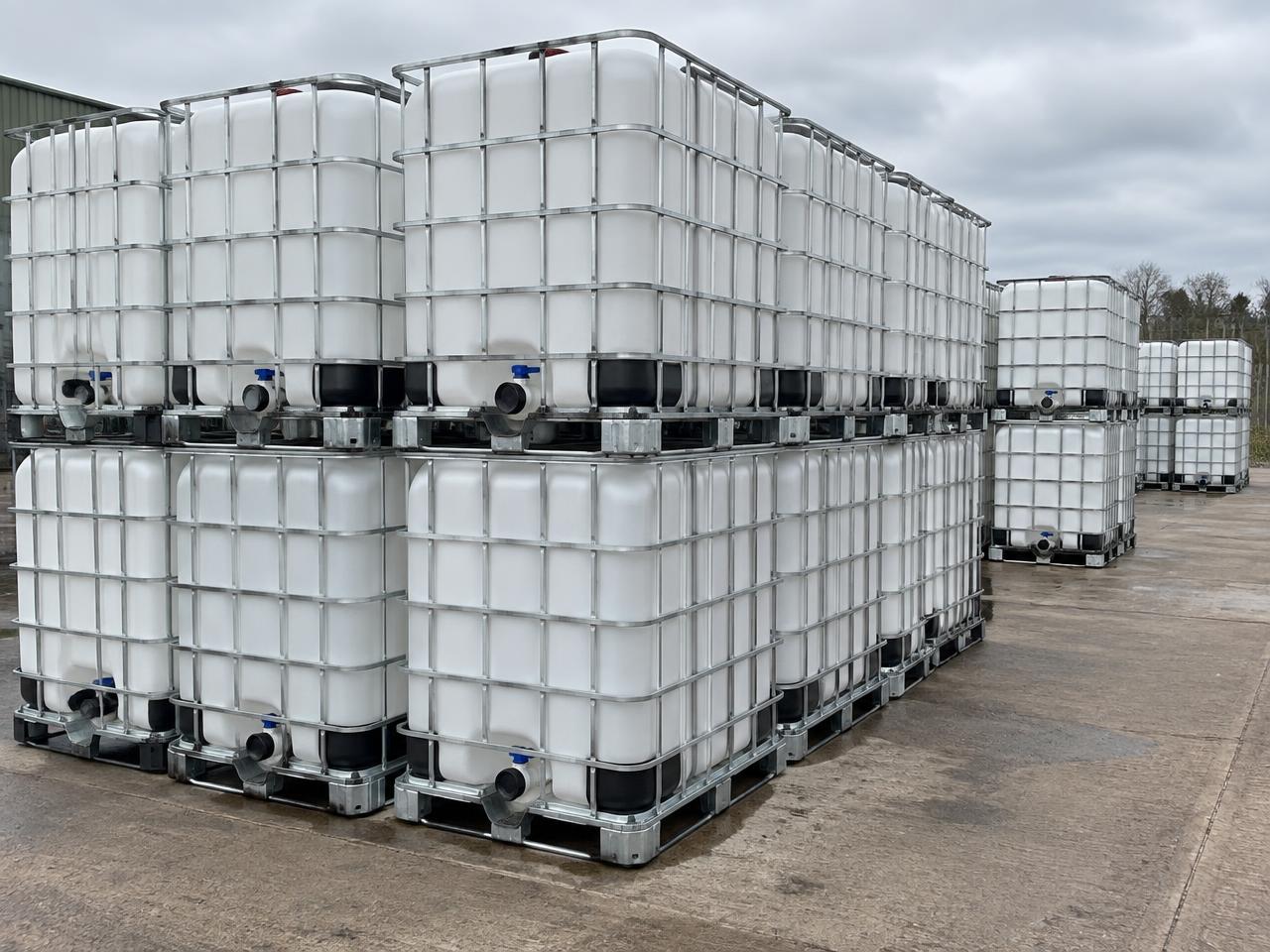 Rows of caged 1000 litre IBC containers stacked in an industrial yard awaiting recycling
